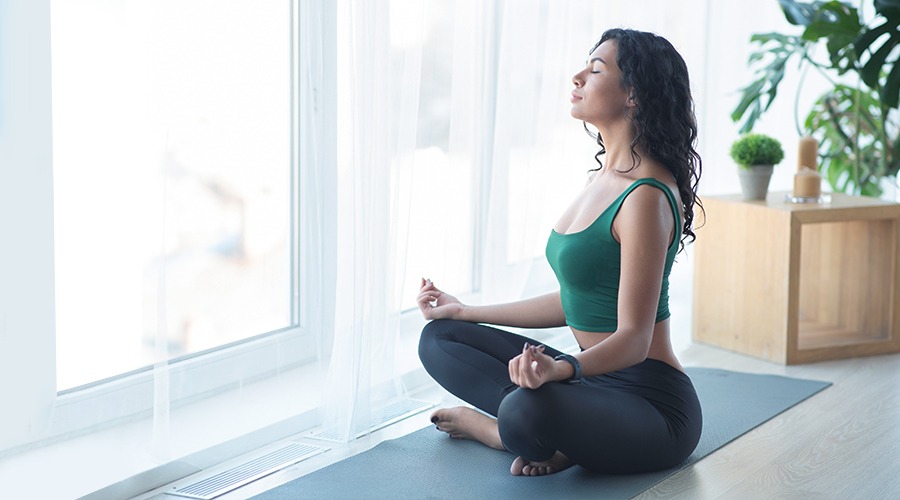 dziewczyna ćwiczy jogę w ciszy przy oknie, co demonstruje wysoki poziom izolacji akustycznej szyby zespolonej