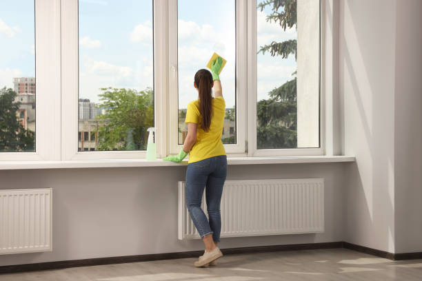kobieta myjąca duże okno po usunięciu resztek kleju metodą z gumką do ścierania